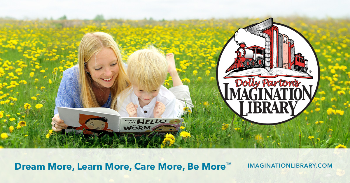 A girl and a boy, lying on their stomachs in a meadow, are reading a book together.