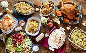 An overhead view of a table filled with traditional Thanksgiving dishes, including a turkey, mashed potatoes, stuffing, green bean casserole, and dinner rolls.