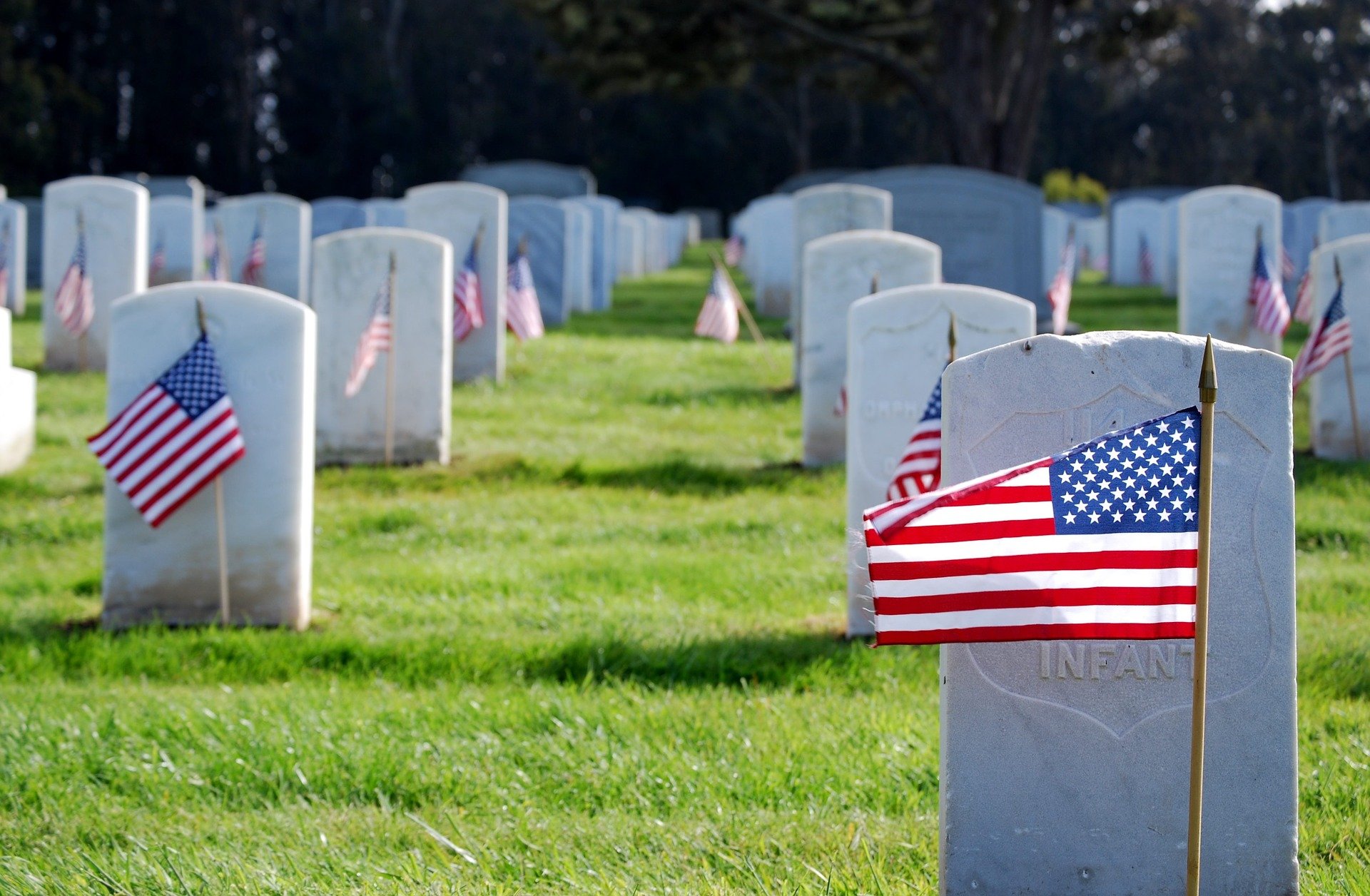 Small American flags are planted in the ground in front of headstones at a military cemetery.