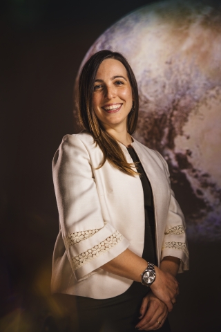 A smiling woman posing in front of an image of a planet.