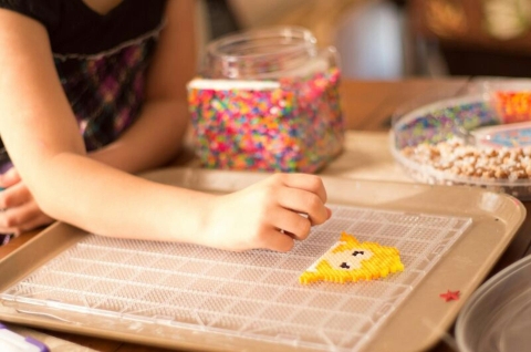 A young person arranging Perler beads on a pegged tray.