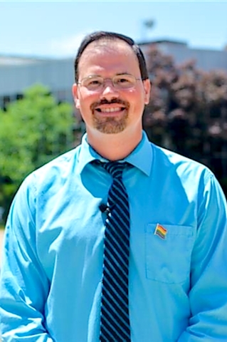 A man with glasses and a beard and mustache is smiling.