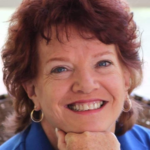 A woman with short, wavy red is smiling while resting her chin on the top of her fist.