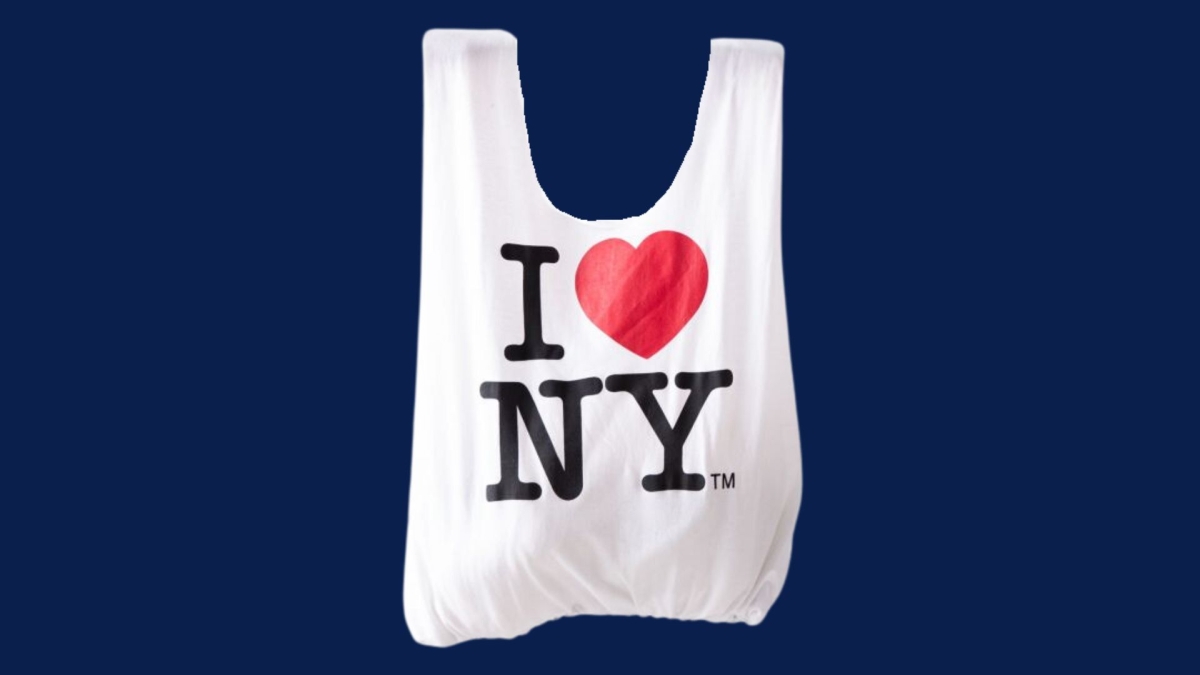 A white tote bag on a navy blue background. The tote bag has "I (heart emoji) NY" on it